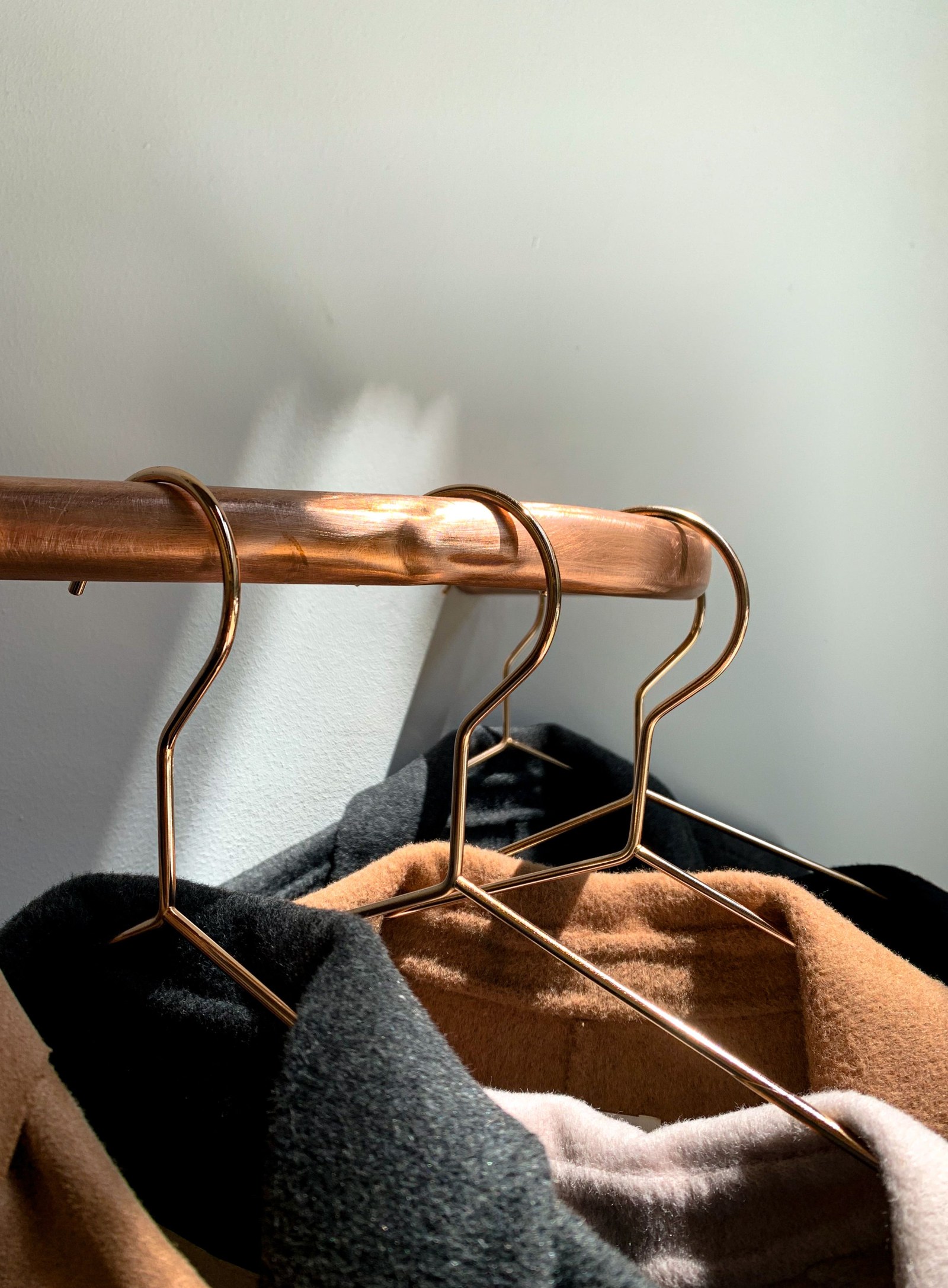 Coats hanging closely together on a copper clothing rail