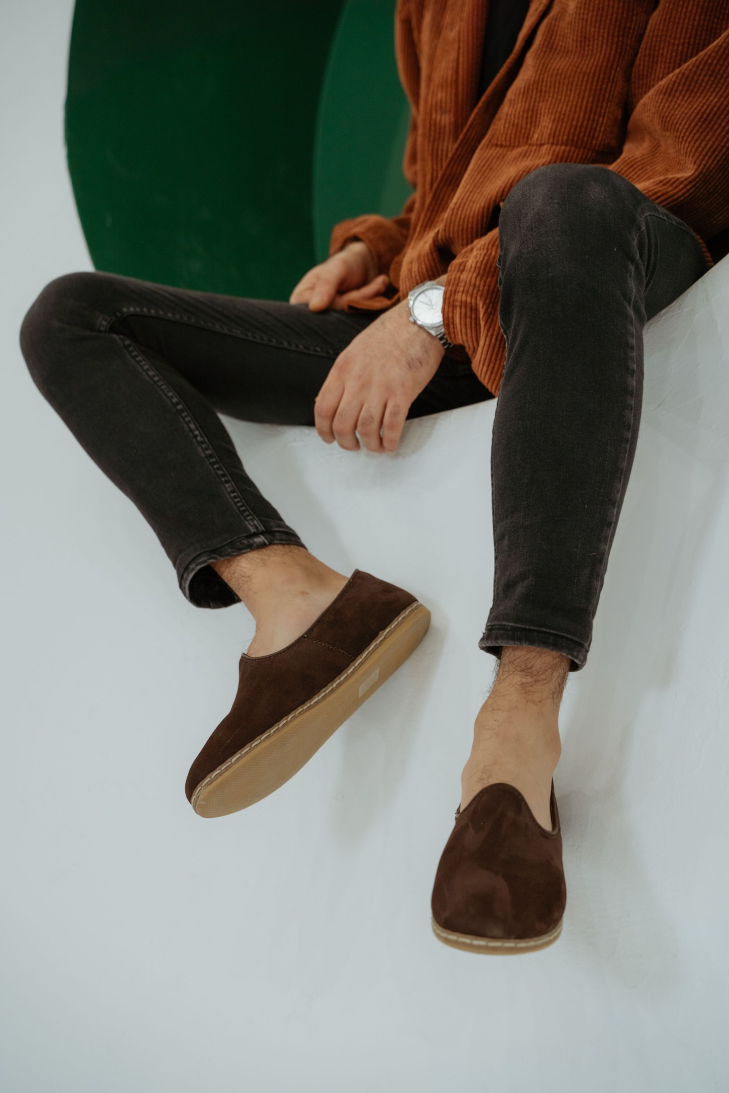 A seated man wearing a relaxed outfit with brown loafers