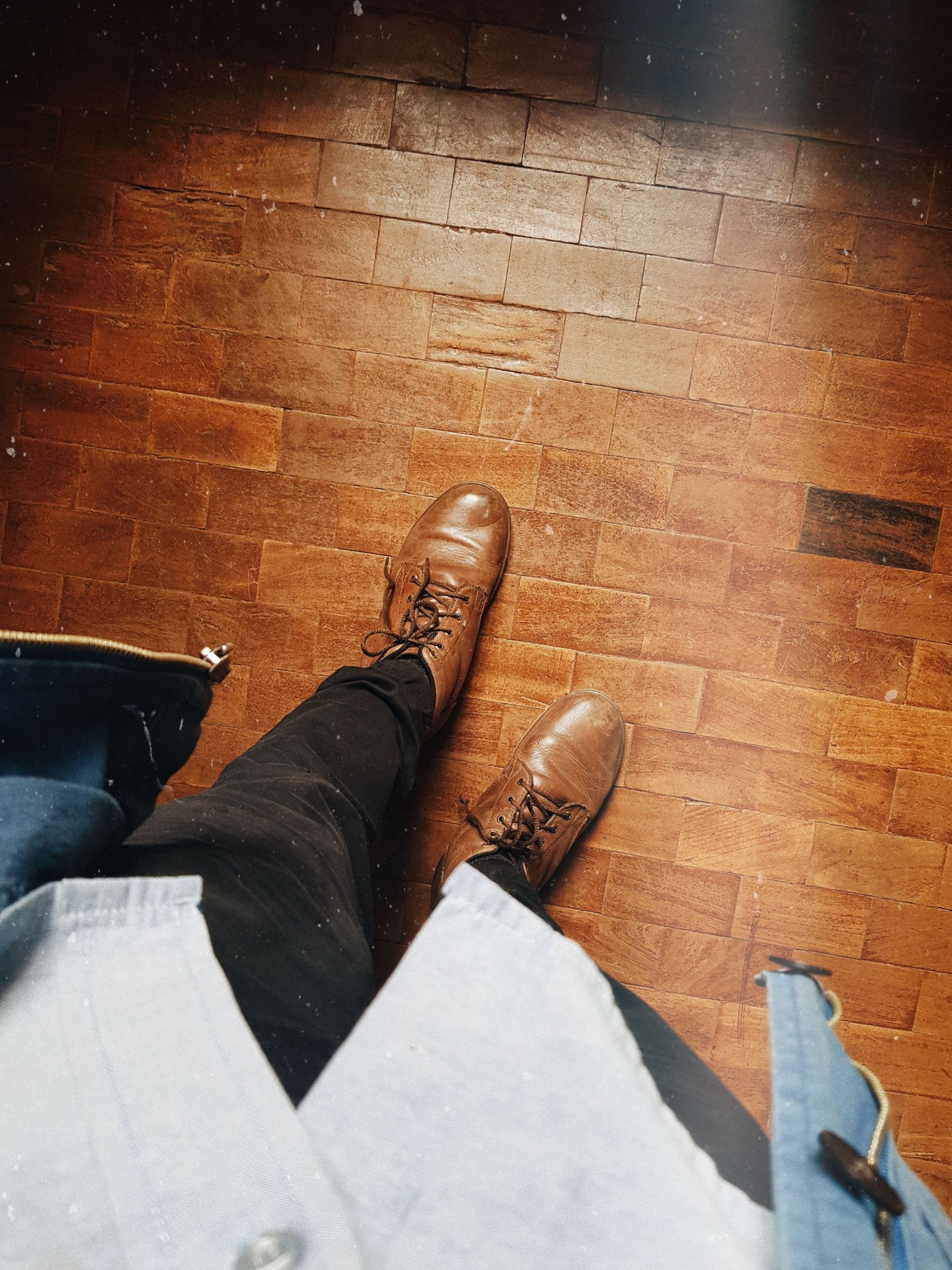 A complete casual outfit viewed toward brown leather shoes on a wooden floor