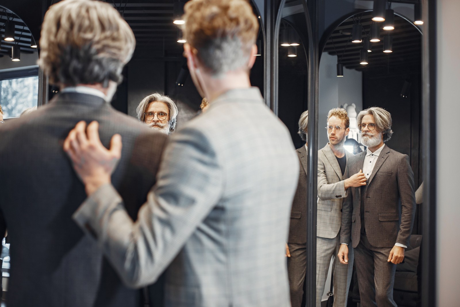 Two men evaluating suits in a boutique mirror