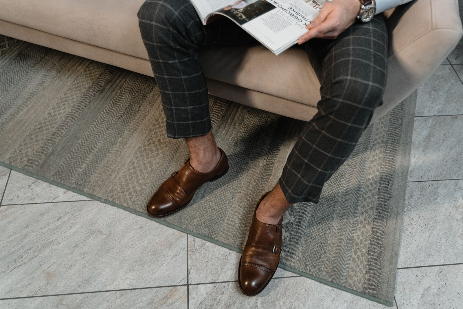A seated man wearing checked trousers and brown shoes